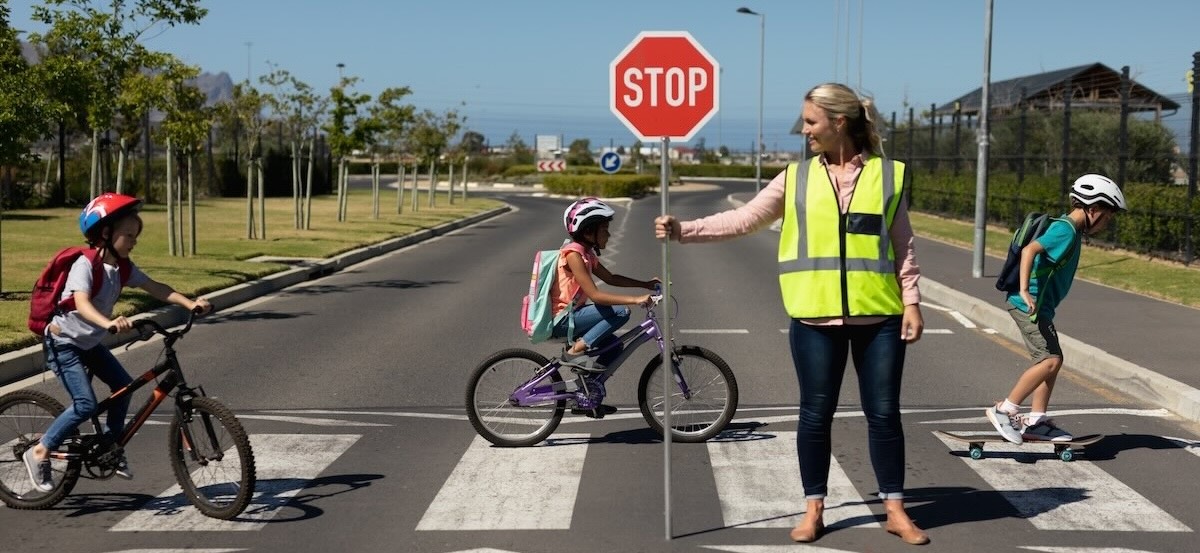 Woman wearing a high visibility vest and holding a stop sign Schoo Crossing